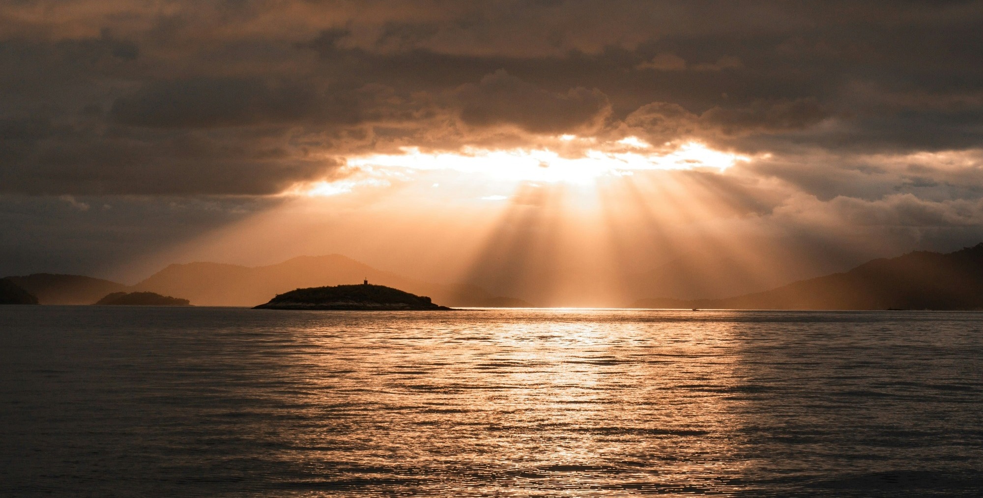 Zonlicht dat door de wolken valt boven rustig water